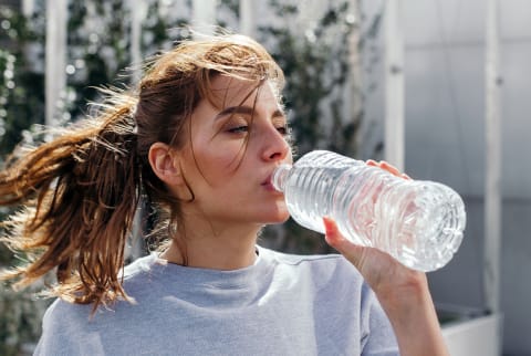 woman drinking from plastic water bottle after working out