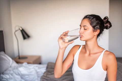 woman sitting on bed drinking water