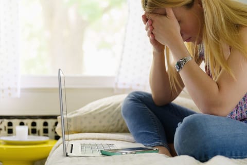 Young woman holding her head in her hands, looking stressed in front of computer