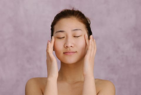 Asian woman with closed eyes touching her temples