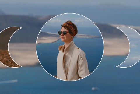 Portrait of beautiful brunette girl with short haircut and headband enjoying of seascape, looking away. Pretty traveler woman in sunglasses and beige trench coat. Islands in ocean on background