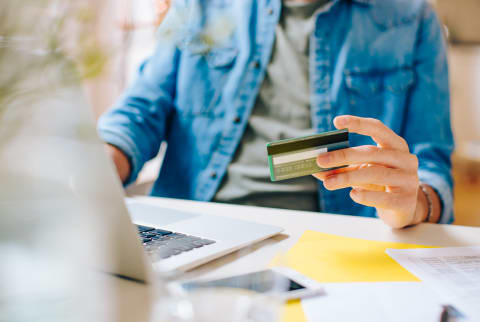 Unrecognizable male using credit card and laptop to pay for online purchases while sitting at table at home