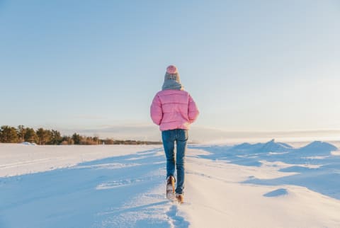 Woman in warm colorful clothes walking in the snow on a frosty sunny day