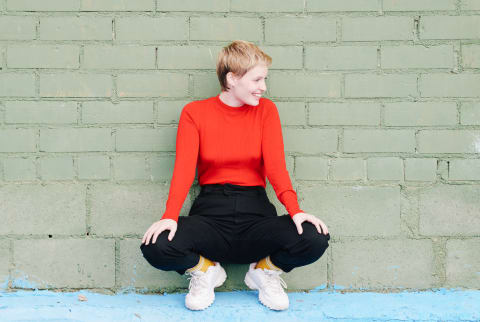 Woman Squatting Down Beside a Green Wall