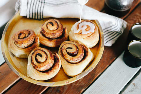 Pouring Icing On Cinnamon Buns On Wooden Table