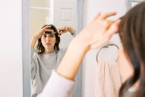 Young Woman Cutting Bangs In Mirror At Home