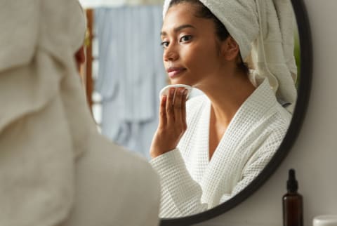 Woman in bathroom removing her make up while looking at the mirror in skincare morning routine at home