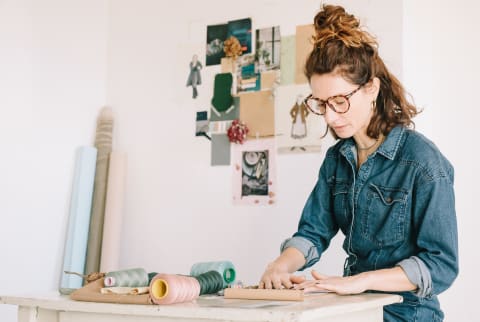 Focused Young Woman Choosing Color Sample For Moodboard On Wooden Table