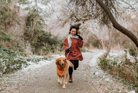 Woman And Dog Running On Snowy Path