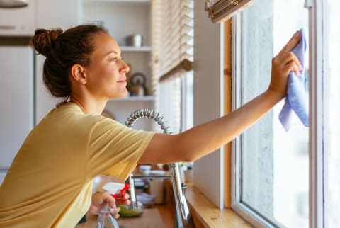 Young Woman Cleaning Window In Kitchen