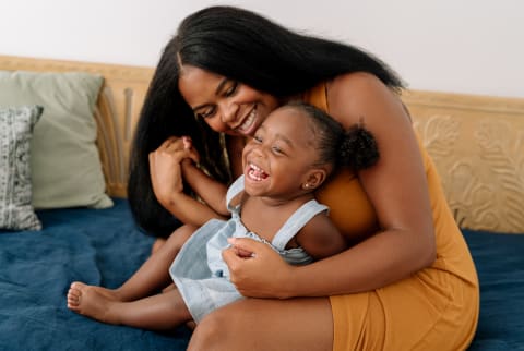 Mama and her happy toddler sitting together on a bed