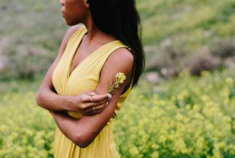 Detail shot of a Black woman holding a yellow flower in a flowery field