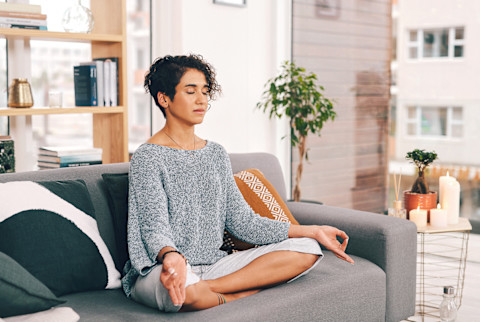 young woman sitting and meditating on her sofa in the living room young woman sitting and meditating on her sofa in the living room