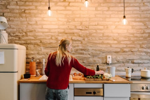  Image #2195144  Uploaded September 22, 2018 8:31 PM  Camera: NIKON D810  RELEASES Has 1 model release  Woman Cooking At Counter In Cozy Kitchen  Back view of young blond woman cooking dinner with vegetables at counter in trendy kitchen with brick wall