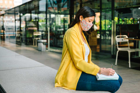 Woman Sitting Outdoors in Business Attire and a Face Mask Journaling