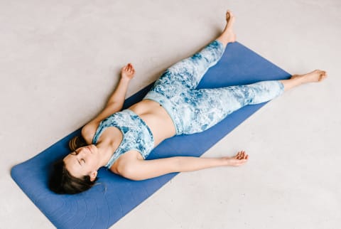 Woman with closed eyes lying in Shavasana pose on concrete floor while doing yoga