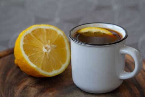A mug of coffee with lemon in it next to half of a lemon