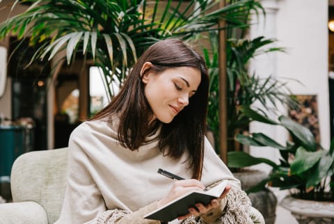 woman sitting on sofa while writing in notebook