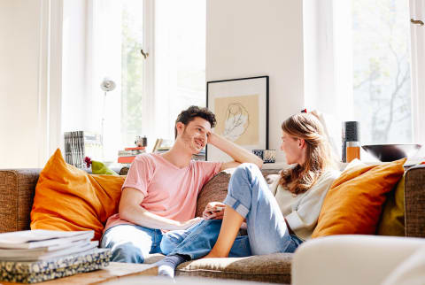 Happy Young Man Talking With Woman On Sofa At Home