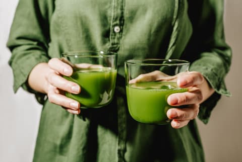 Woman Holding Two Glasses of Green Juice/Smoothies Woman Holding Two Glasses of Green Juice/Smoothies