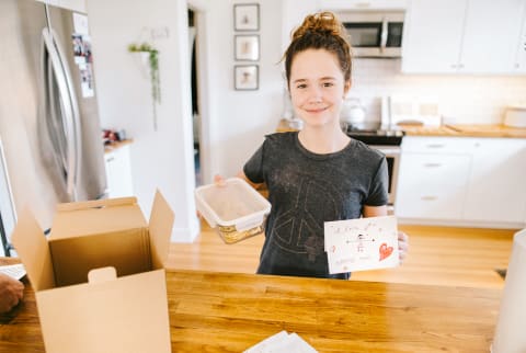 Girl Holding a Container of Baked Goods and a Handwritten Card For a Care Package