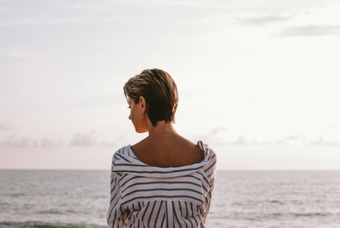 Image of a woman looking out at the ocean thinking.