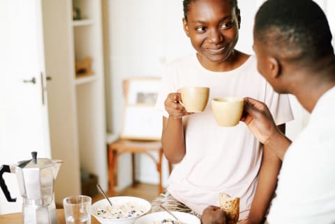 woman sitting in kitchen with her boyfriend, having tasty healthy breakfast, drinking coffee and smiling cheerfully