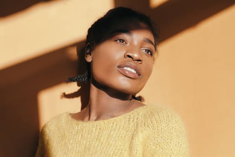 black woman leaning against wall wearing a yellow sweater with sun shining