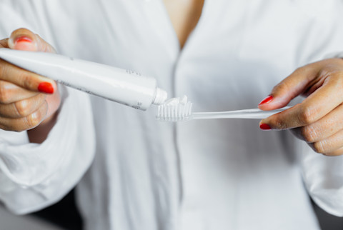 Woman with red nails putting toothpaste on a toothbrush Woman with red nails putting toothpaste on a toothbrush