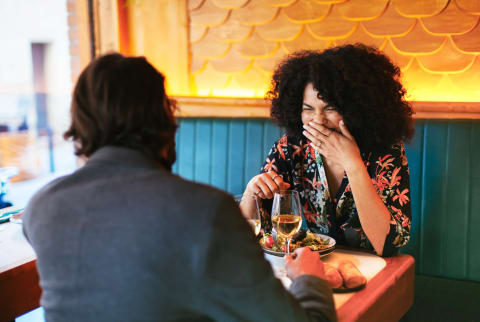 woman with hand over mouth on a date with a man at a restaurant 