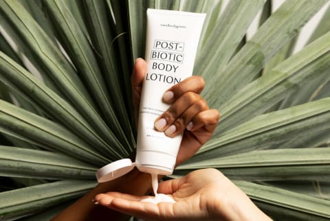 One hand squeezing postbiotic body lotion into another hand