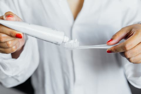 Woman with red nails putting toothpaste on a toothbrush