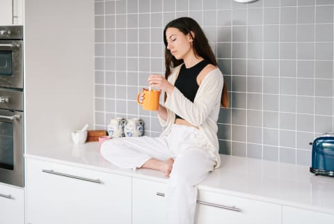 Woman Sitting on Kitchen Counter Drinking Tea/Coffee