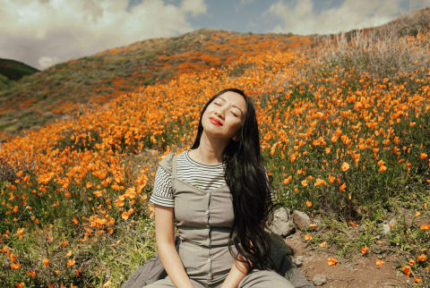 Woman Sitting on a Hillside, Eyes Closed, Enjoying the Sun