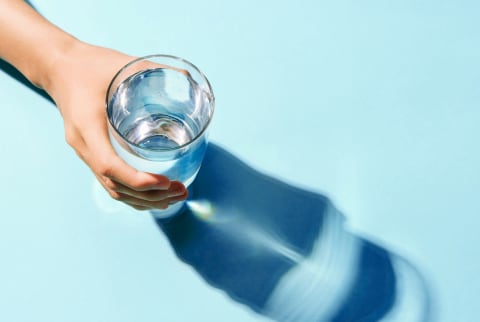 Hand holding water glass in strong lighting against minimal blue seamless