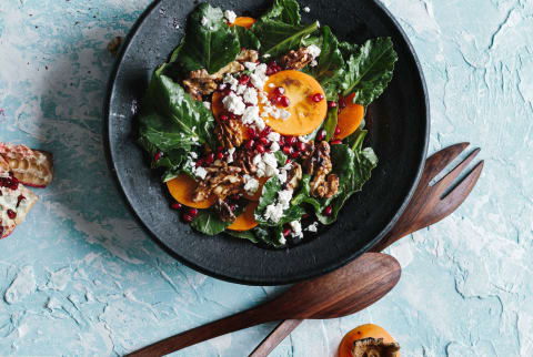 Winter / fall kale salad topped with persimmon, walnut, pomegranate arils, and crumbled cheese