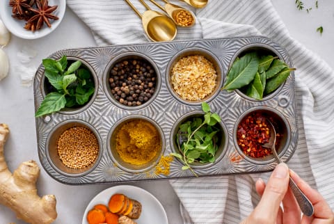 Ginger, turmeric, mint, peppercorn, crushed red pepper, bay leaves, star anise, and turmeric with hand, spoon, and linen