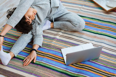 Woman stretching and doing yoga in front of computer laptop screen on rug indoors