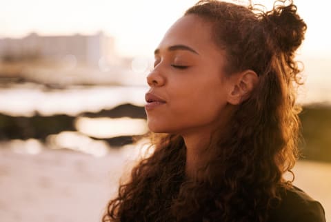 Shot of an attractive young woman sitting alone on a mat and meditating on the beach at sunset stock photo