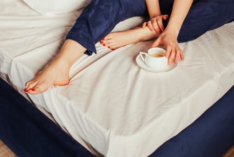 Woman With Cup Of Coffee On Bed showing toes