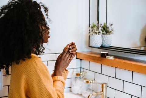 Black woman millennial looking in mirror during fall / winter in modern, white bathroom