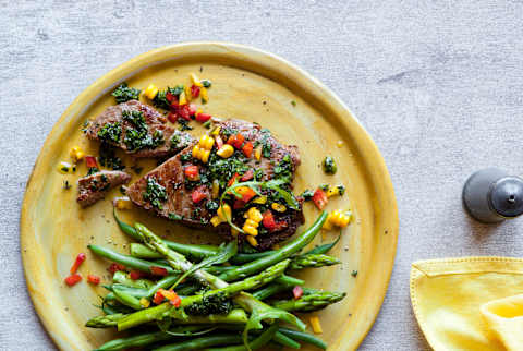 Overhead of steak with chimichurri, corn, and peppers with asparagus on yellow plate Overhead of steak with chimichurri, corn, and peppers with asparagus on yellow plate
