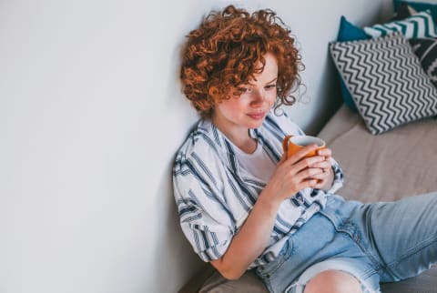 Woman Sitting on a Bed Thinking With a Cup of Coffee