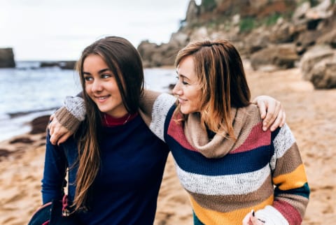 Woman / mom with her arm around her teenage daughter outside on the beach during fall / winter!