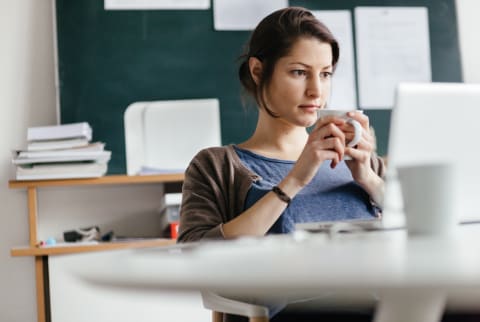 woman sitting at her desk at work with coffee looking overwhelmed