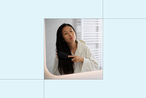 image of woman brushing her hair in the mirror on light blue background