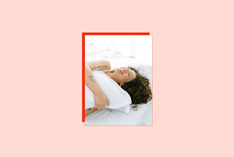 image of woman laying on bed hugging pillow on light peach background image of woman laying on bed hugging pillow on light peach background