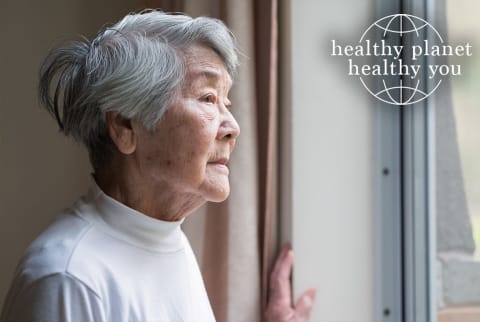 Older Chinese woman looks out window with Healthy Planet Healthy You Logo