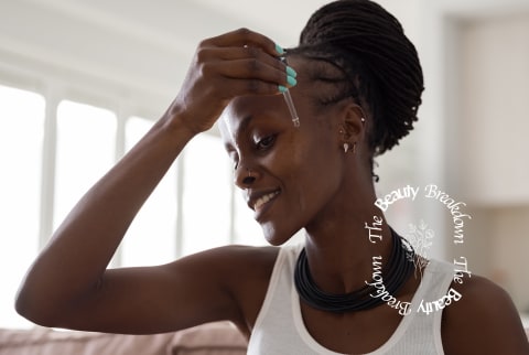 a black woman applies serum to her face using a dropper