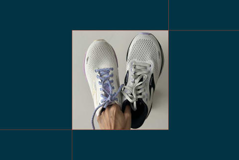 picture of hand holding one brooks ghost shoe and one brooks adrenaline shoe on blue background